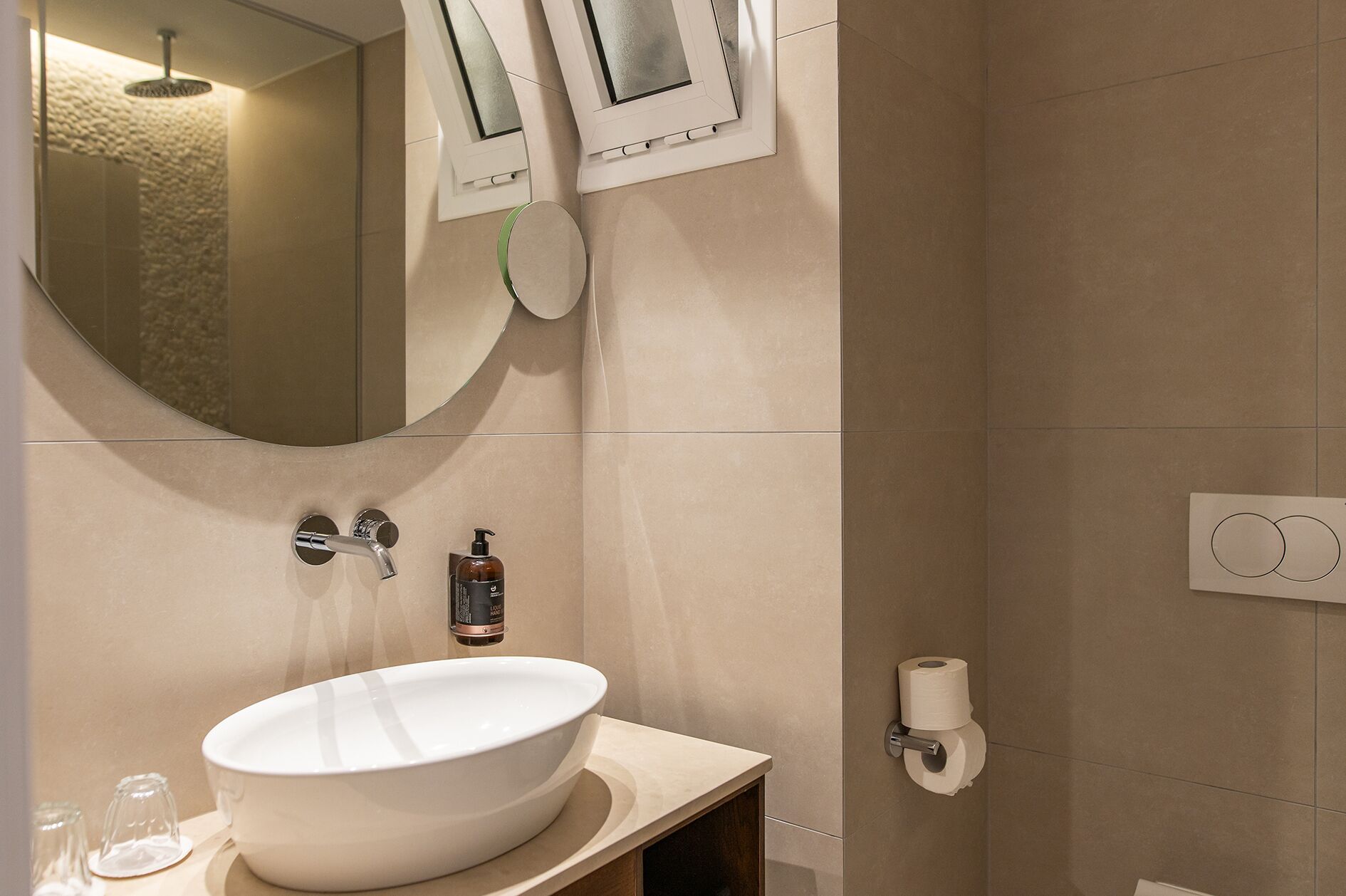 A bathroom with a large oval sink, a mirror, a handheld showerhead, and a toilet paper holder.