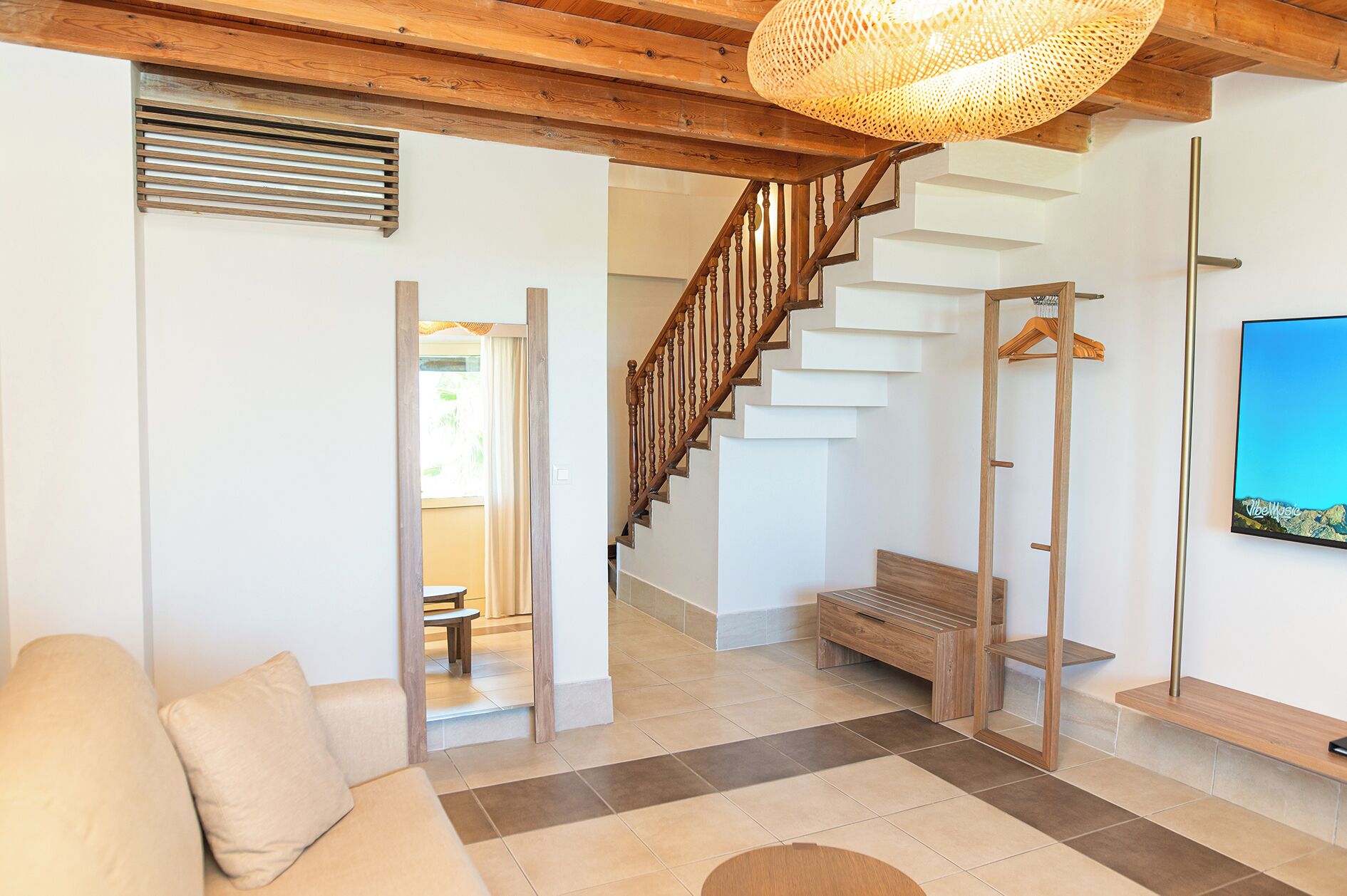 Un interior moderno con una escalera de madera, un sofá, un banco y una lámpara colgante.