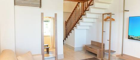Un interior moderno con una escalera de madera, un sofá, un banco y una lámpara colgante.