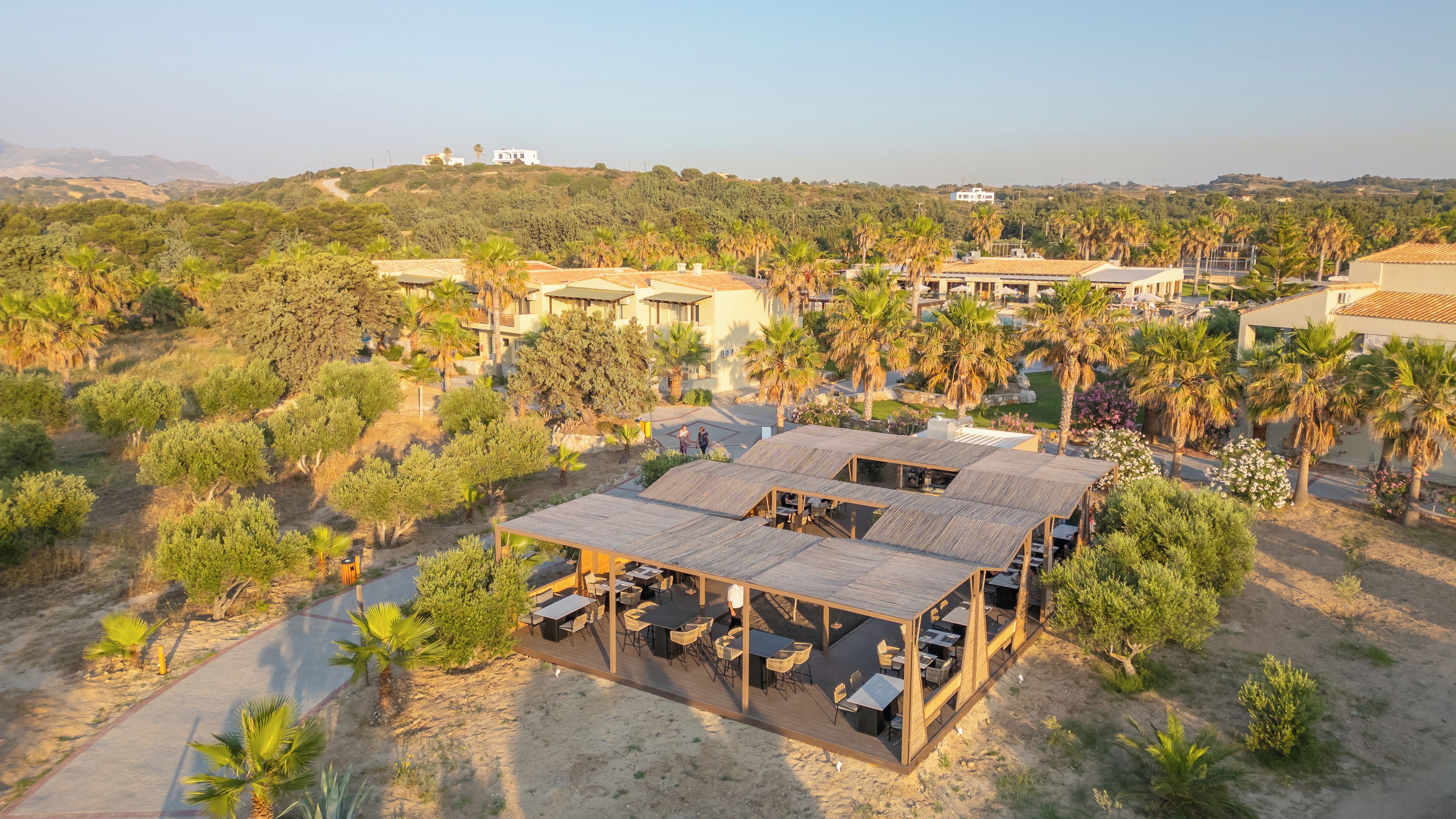 Un resort con zonas de estar al aire libre, rodeado de palmeras y follaje, con vistas a un paisaje montañoso.