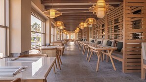Amplio espacio interior con mesas y sillas largas, estanterías de madera y lámparas colgantes de mimbre.