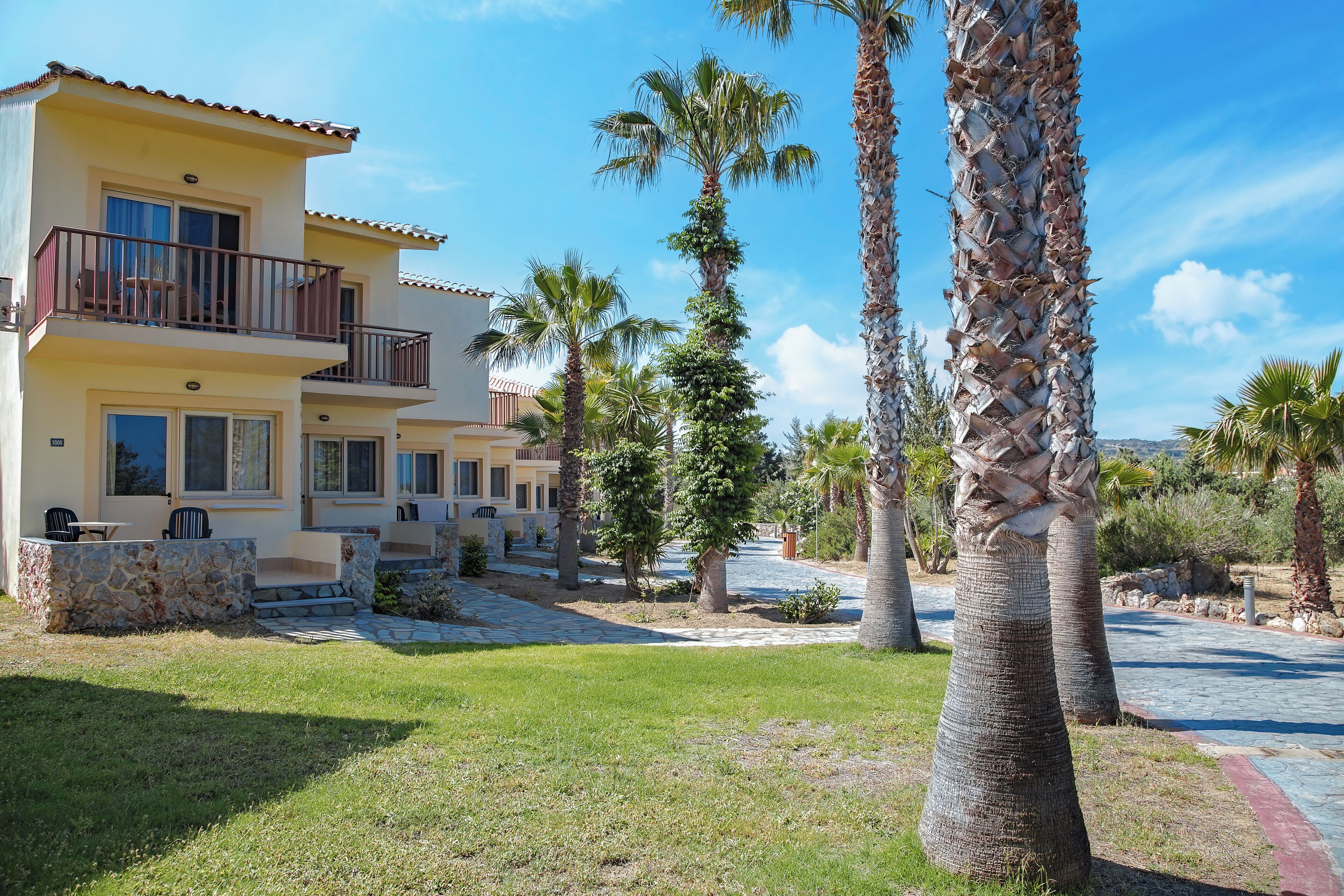 A two-story building with a balcony, surrounded by palm trees and a stone pathway.