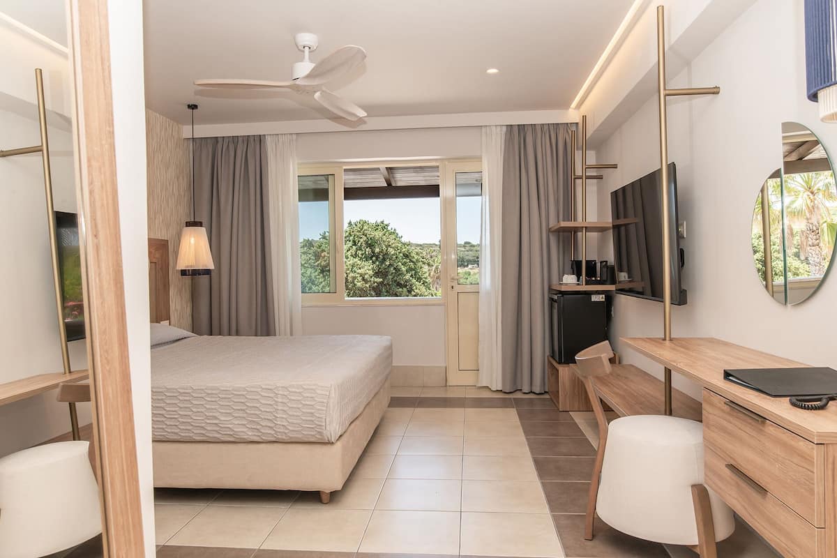 Ein Hotelzimmer mit Bett, Schreibtisch, Stuhl, Fernseher und Deckenventilator.
