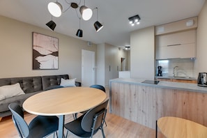 A modern kitchen with a wooden island, a dining area with a round table and chairs, and a grey sofa.