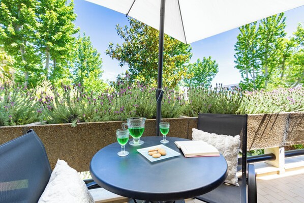 A round table with a chair, a glass of green drink, a plate with cookies, and a book.