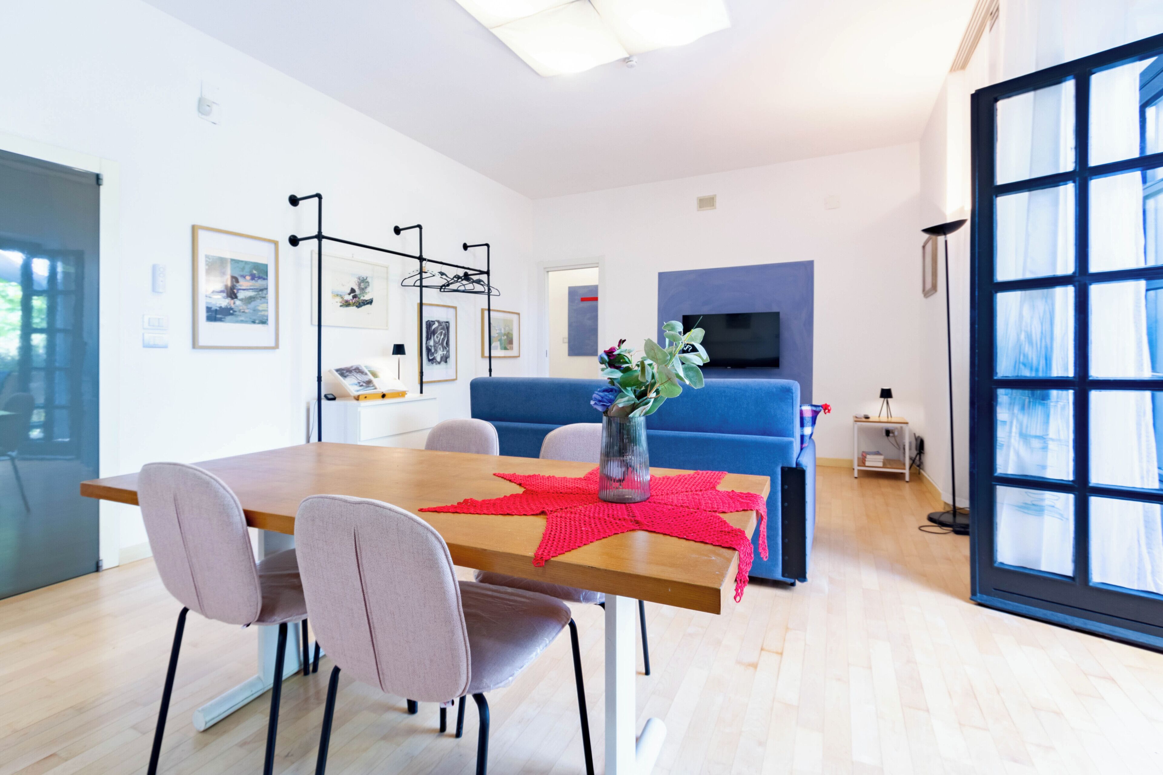 Un salon moderne avec une table à manger, des chaises, un canapé bleu, un téléviseur et une grande fenêtre.