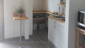 Een moderne keuken met witte kastjes, een houten aanrecht en een spoelbak. Er staat een plantje op een klein tafeltje en een klok hangt aan de muur.