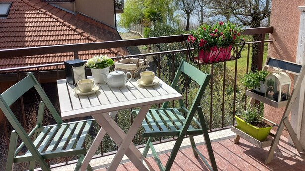 Een terras met een tafel en stoelen, een uitzicht op een meer en een gebouw met een pannendak.