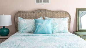 A bed with a woven headboard, a teal lamp, and a mirror on a dresser.