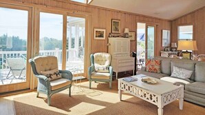 Un salon spacieux avec des boiseries, de grandes fenêtres, une table basse blanche et des sièges confortables.