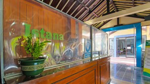 A reception area with a wooden counter, a potted plant, and a glass wall with the name "Iotana" visible. - OYO 1984 Hotel Istana Family Syariah (Nganjuk)