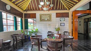A lobby with wooden ceiling beams, a chandelier, and a tiled floor. There are several wooden chairs and tables, some with plants. A clock and framed certificates are on the walls. - OYO 1984 Hotel Istana Family Syariah (Nganjuk)