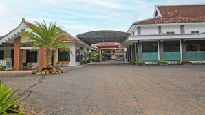 A hotel entrance with a gravel driveway, a covered walkway, and a palm tree. - OYO 1984 Hotel Istana Family Syariah (Nganjuk)