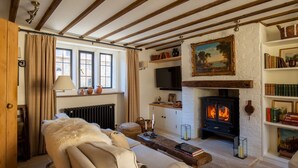 A cozy living room with a fireplace, a sofa, a television, and a bookshelf. - Little Oakley Cottage - sleeps 4 guests  in 2 bedrooms (Sandford St Martin)