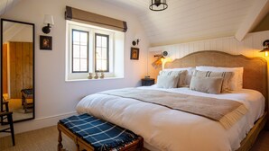 A bedroom with a large bed, a bench, a dresser, a mirror, and two windows with curtains. - Little Oakley Cottage - sleeps 4 guests  in 2 bedrooms (Sandford St Martin)