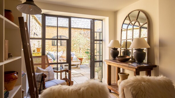 A cozy room with a large window, a wooden chair, a table with lamps, and a bookshelf. - Little Oakley Cottage - sleeps 4 guests  in 2 bedrooms (Sandford St Martin)