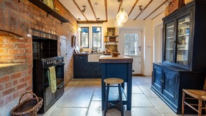A kitchen with a brick wall, a black stove, a wooden island, and a dark blue cabinet. - Little Oakley Cottage - sleeps 4 guests  in 2 bedrooms (Sandford St Martin)