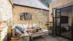 A cozy outdoor seating area with a stone wall, a wooden bench, and a cushioned sofa. - Little Oakley Cottage - sleeps 4 guests  in 2 bedrooms (Sandford St Martin)