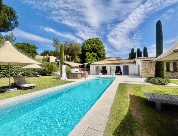 A swimming pool with a clear blue water, surrounded by a well-maintained lawn and a stone building with a tiled roof.