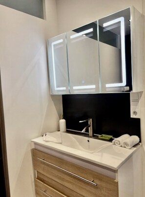A bathroom with a white sink, a mirror with a light, and a wooden cabinet below.