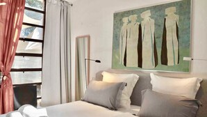 Een hotelkamer met een groot bed, twee kussens, een schilderij aan de muur en een raam met gordijnen.