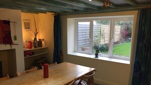 A dining area with a wooden table and chairs, a window with a view of a garden, and a ceiling with exposed beams.