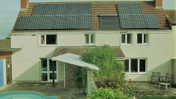 A two-story house with solar panels on the roof, a swimming pool, and a garden area with a patio.