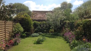 A well-maintained garden with a variety of flowering plants and a neatly trimmed lawn, leading to a house with a tiled roof.