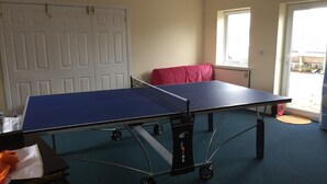A room with a ping pong table, a red couch, and a door.