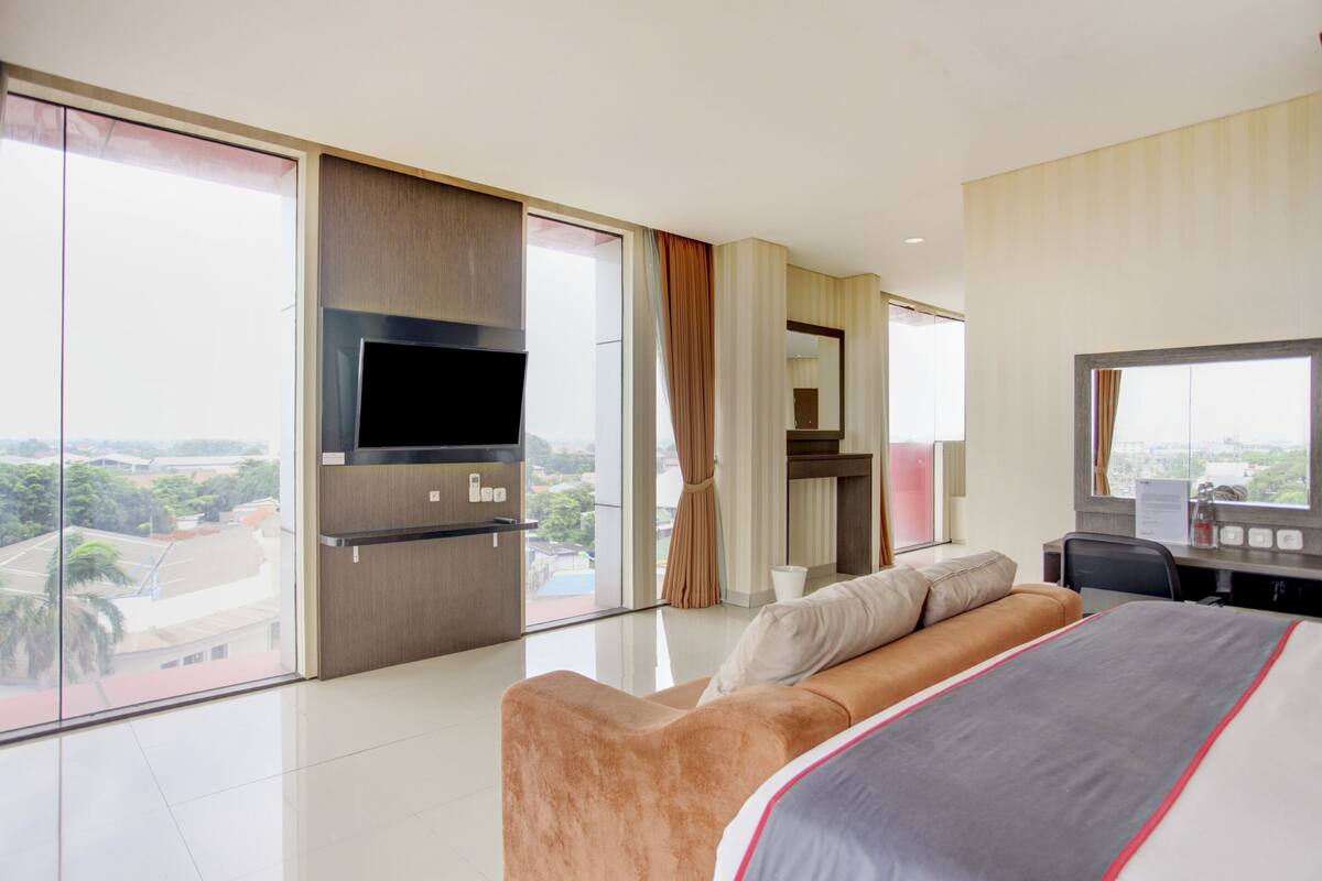 Habitació d'hotel moderna amb un llit gran, una televisió de pantalla plana, un escriptori amb cadira i vistes a la ciutat a través de grans finestres.