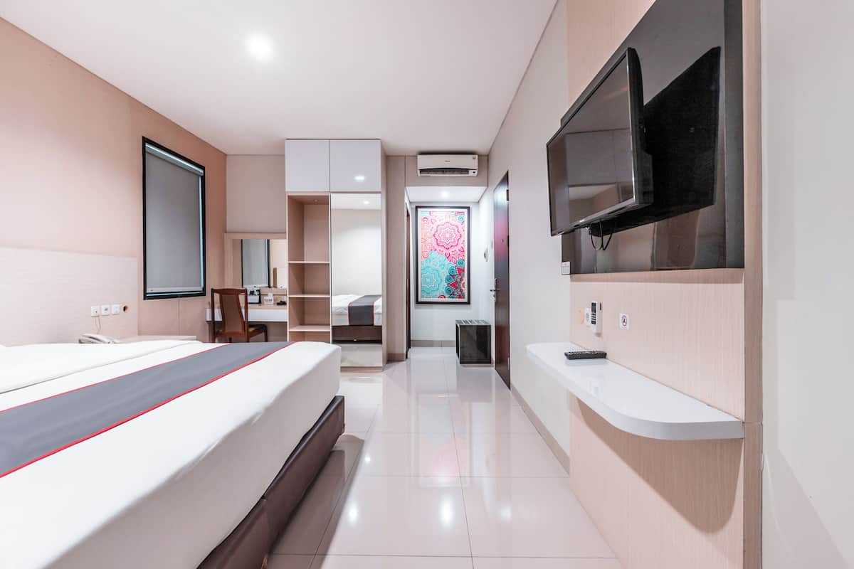A modern hotel room with a bed, a TV mounted on the wall, a desk, and a bathroom.