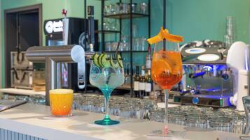 Zona de bar con mostrador que exhibe tres bebidas, una máquina de café y un estante con copas.