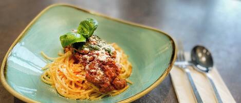 A plate of spaghetti with tomato sauce and a basil leaf garnish on a ceramic plate.