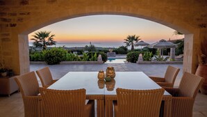 An outdoor dining area with wicker chairs and a table, overlooking a landscaped garden and a pool. - Villa Elia, By Hellocrete (Asteri village)