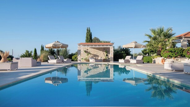A swimming pool with lounge chairs and umbrellas, surrounded by greenery and a stone structure. - Villa Elia, By Hellocrete (Asteri village)
