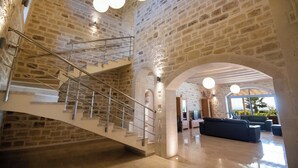 A spacious interior with a stone wall, a staircase with metal railings, and a modern living area with a sofa and a TV. - Villa Elia, By Hellocrete (Asteri village)