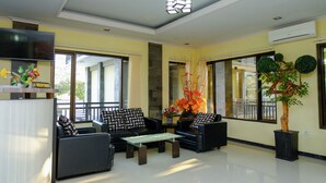 A spacious living room with a black sofa set, a coffee table, and a large window offering a view of the outside. - Capital O 887 Green Hill Hotel And Convention Center (Jombang)