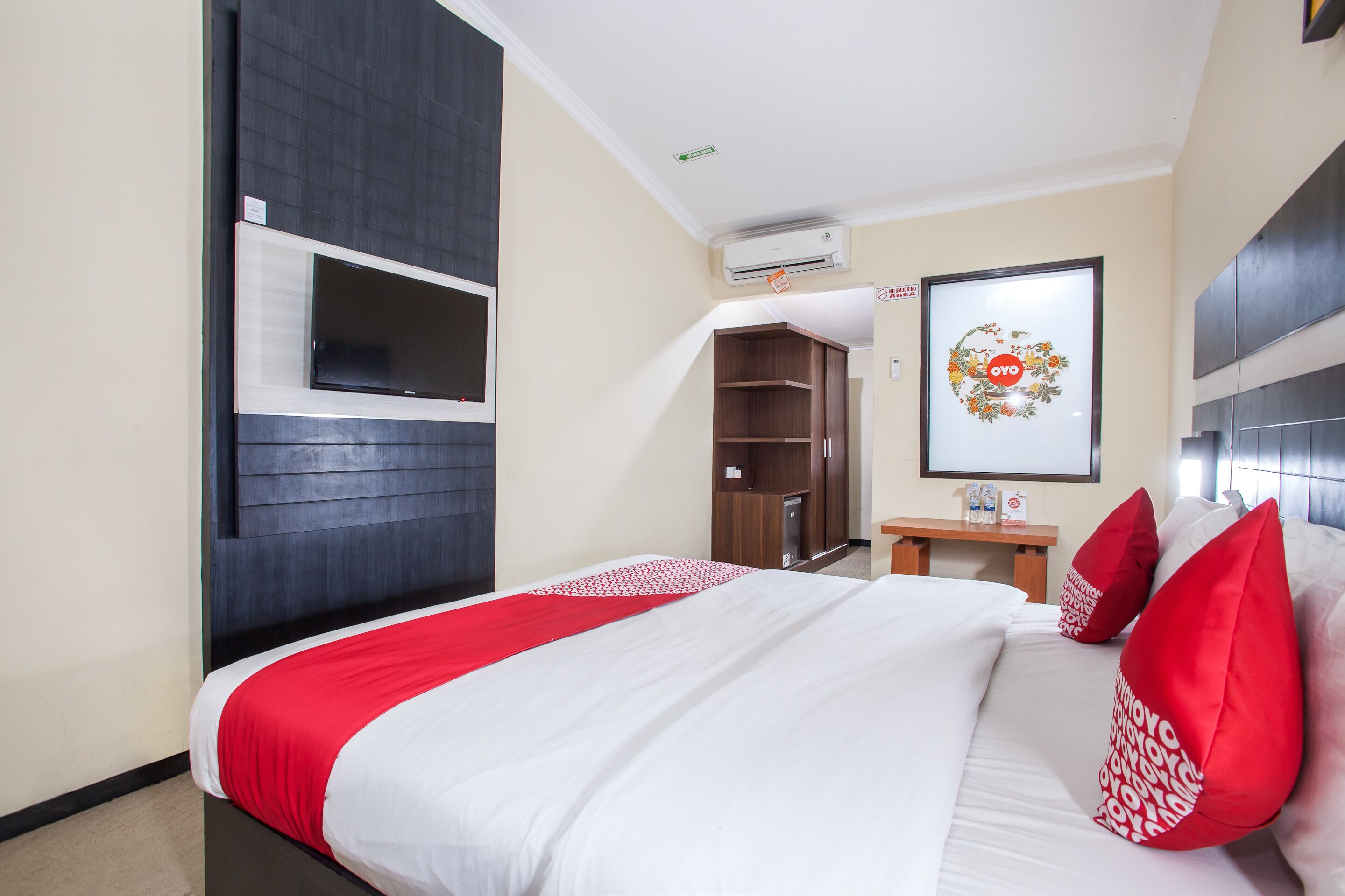 Een hotelkamer met een bed, een aan de muur bevestigde televisie, een kledingkast en een klein tafeltje met een spiegel.