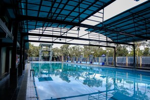 A swimming pool with a glass ceiling, surrounded by trees and a covered area. - Capital O 887 Green Hill Hotel And Convention Center (Jombang)