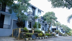 A modern residential building with multiple balconies, a brick pathway, and surrounding greenery. - Capital O 887 Green Hill Hotel And Convention Center (Jombang)