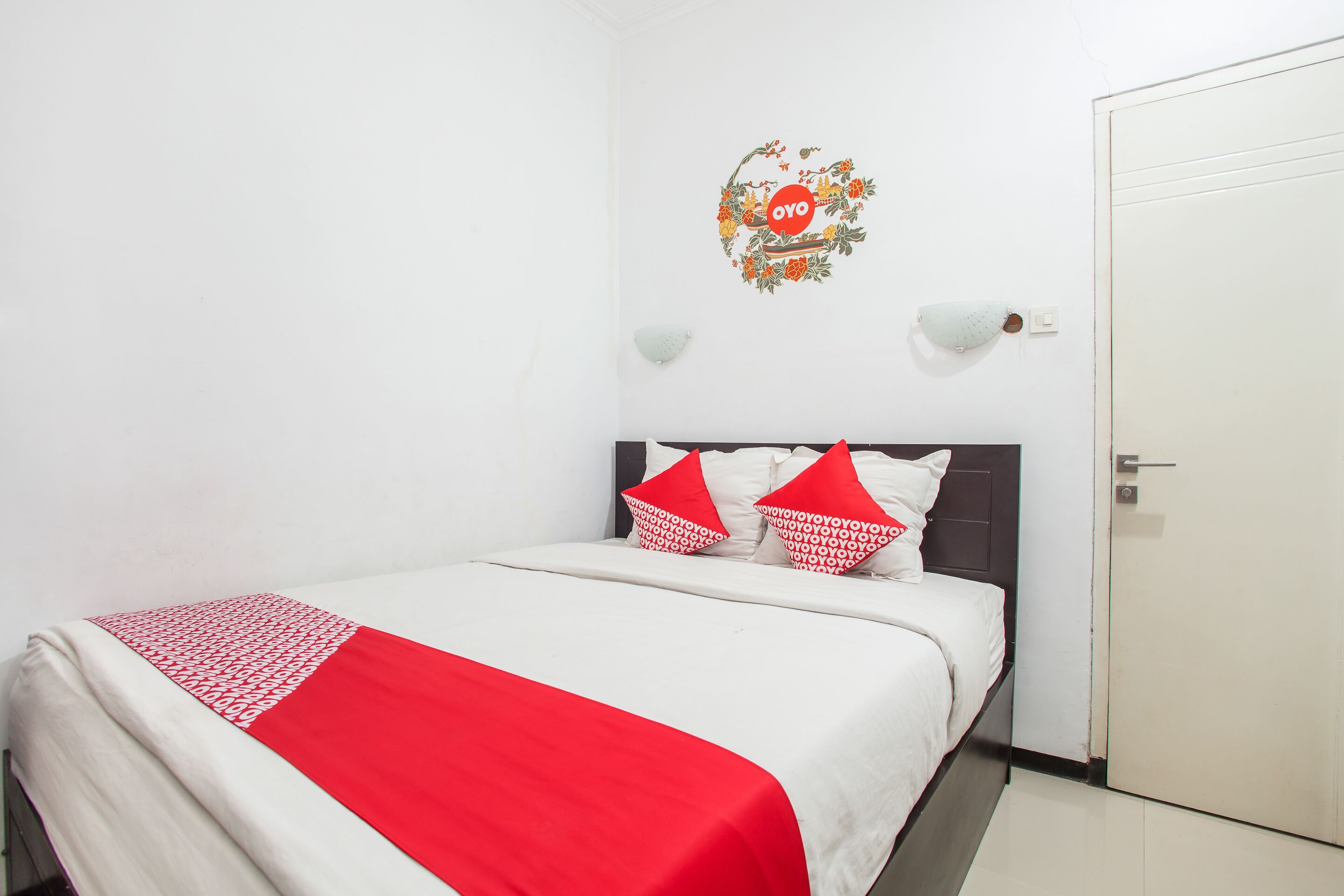 Camera d'albergo con un letto, pareti bianche, una porta e un addobbo murale.