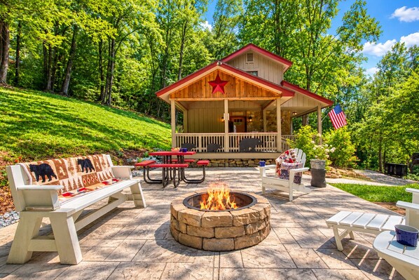 A lodge with a stone fire pit, outdoor seating, and a porch with a red roof and American flag. - Rambling Bear on Cove Creek, Hot Tub, WIFI, $560 FREE tickets each paid day!!! (Sevierville)