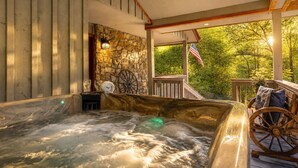 Un jacuzzi con un muro de piedra de fondo, una terraza de madera y vistas a la vegetación.