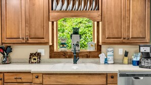 Una cocina con armarios de madera, un lavavajillas de acero inoxidable y un ventanal con vistas a zonas verdes.