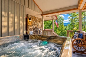 A hot tub with a stone wall backdrop, a wooden deck, and a view of trees and mountains. - Rambling Bear on Cove Creek, Hot Tub, WIFI,  $560 FREE tickets each paid day!!! (Sevierville)