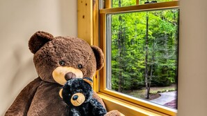 Un oso de peluche marrón grande y un oso de peluche negro más pequeño sentados junto a una ventana con vistas a un bosque.