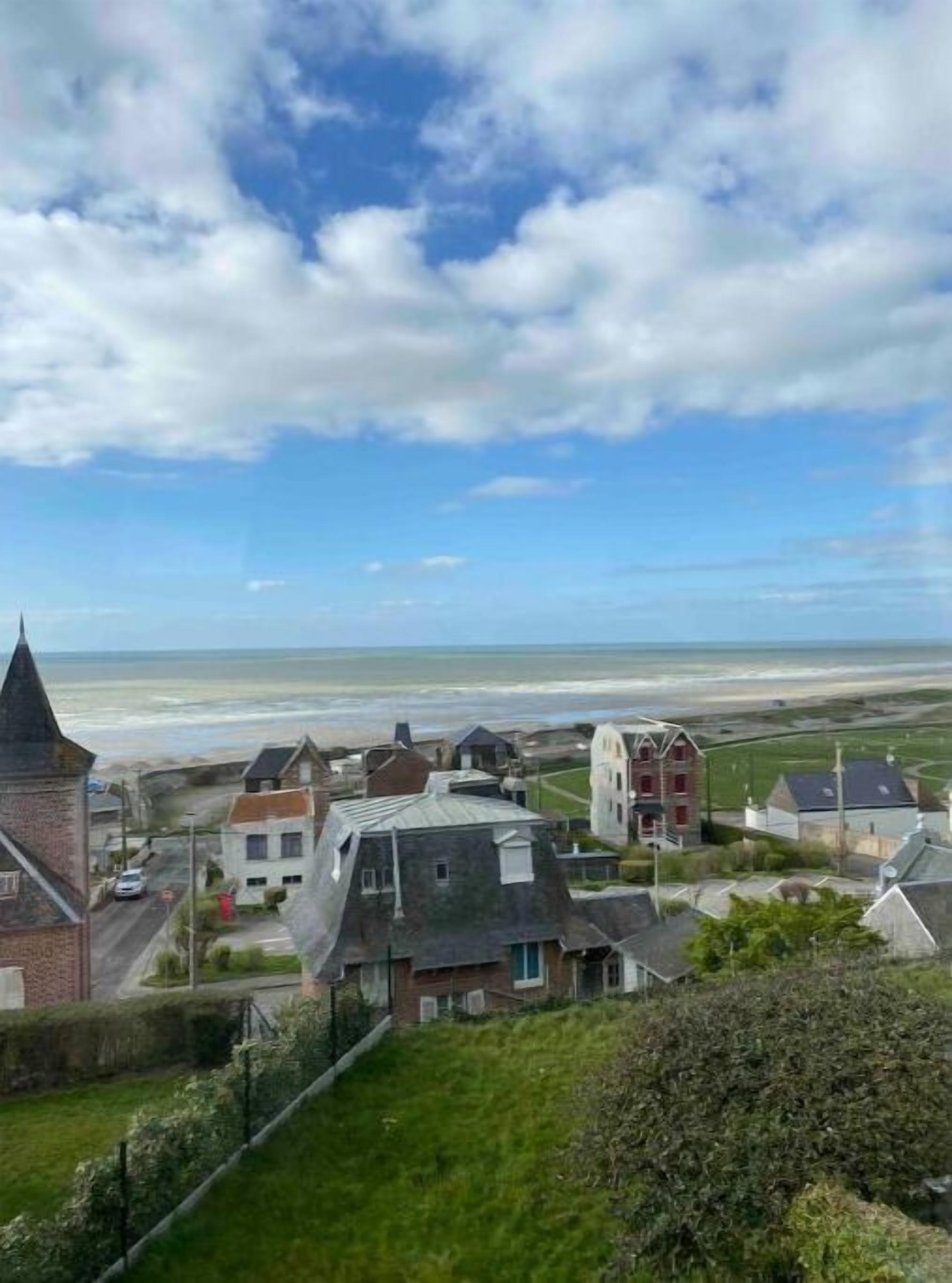 A coastal town with a prominent church spire, residential buildings, and a beach in the background.