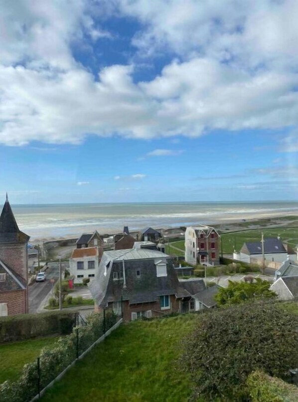 Eine Küstenstadt mit einem markanten Kirchturm, Wohnhäusern und einem Strand im Hintergrund.