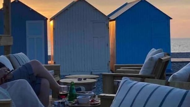 A beachside seating area with lounge chairs and a table, overlooking the ocean with beach huts in the background. - Apartment for 2 people - Ocean view😍 (Woignarue)