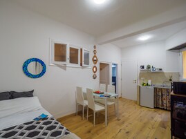 Un espacio habitable compacto con cama, una mesa de comedor con sillas, kitchenette y baño pequeño.
